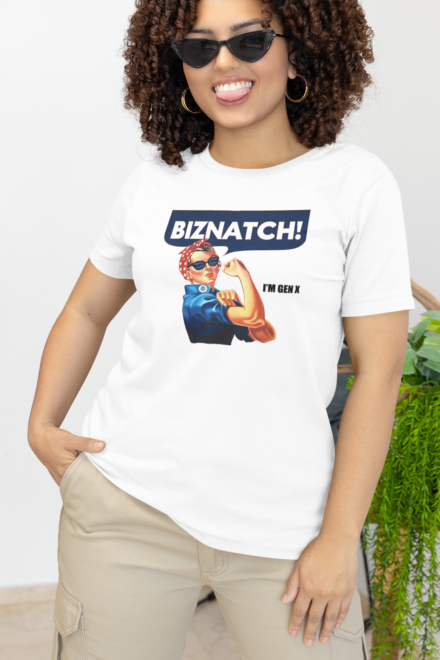 Curly haired woman wearing sun glasses, sticking her tounge out, wearing the Rosie the Riveter sytled T-Shirt that states "Biznatch! I'm Gen X".